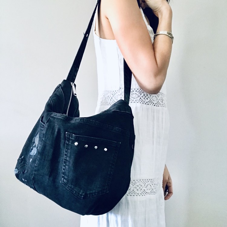 Woman in white dress carrying a black denim hobo bag on her shoulder